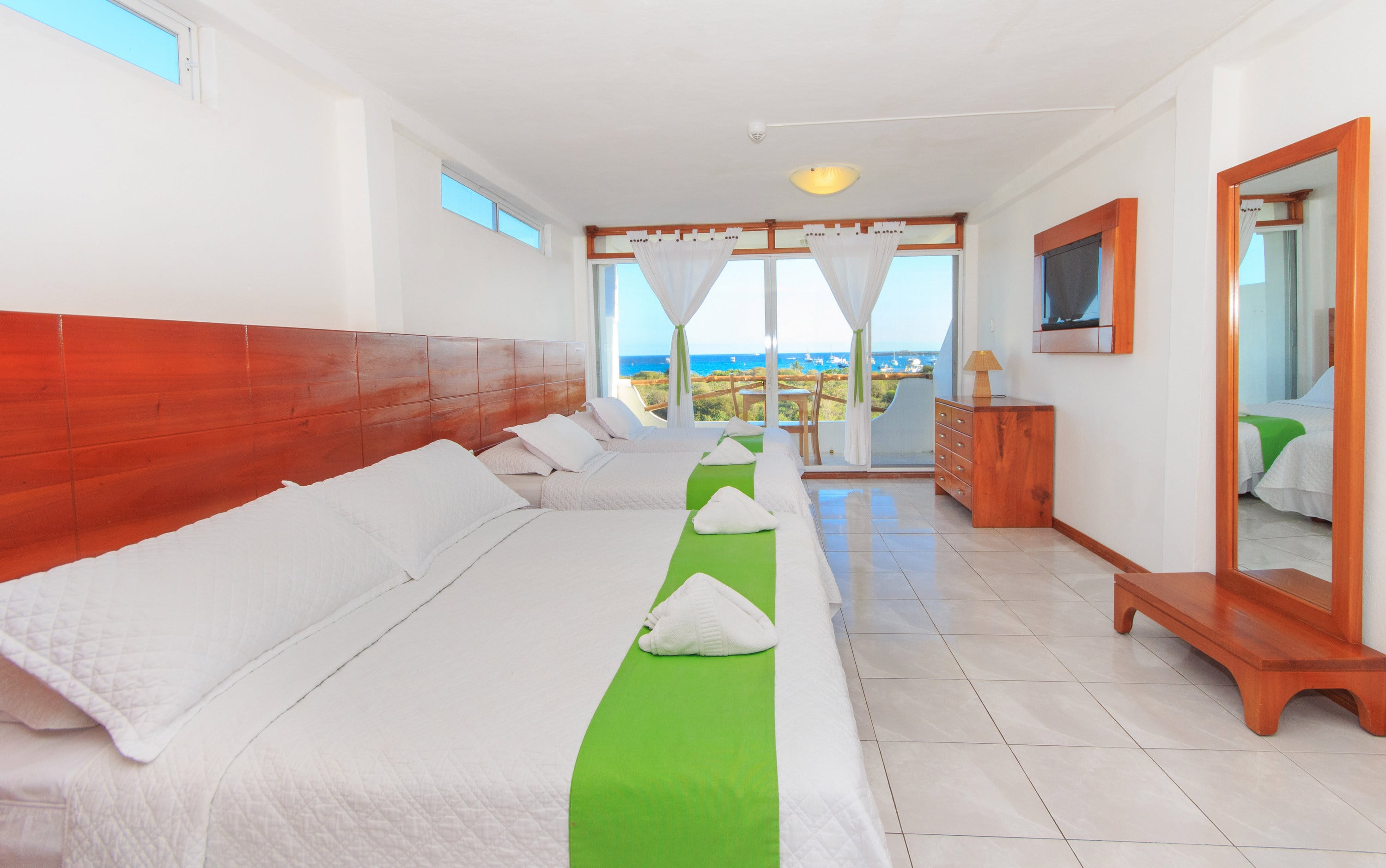 Triple-bed room with three beds, a mirror, ocean view, and a TV.